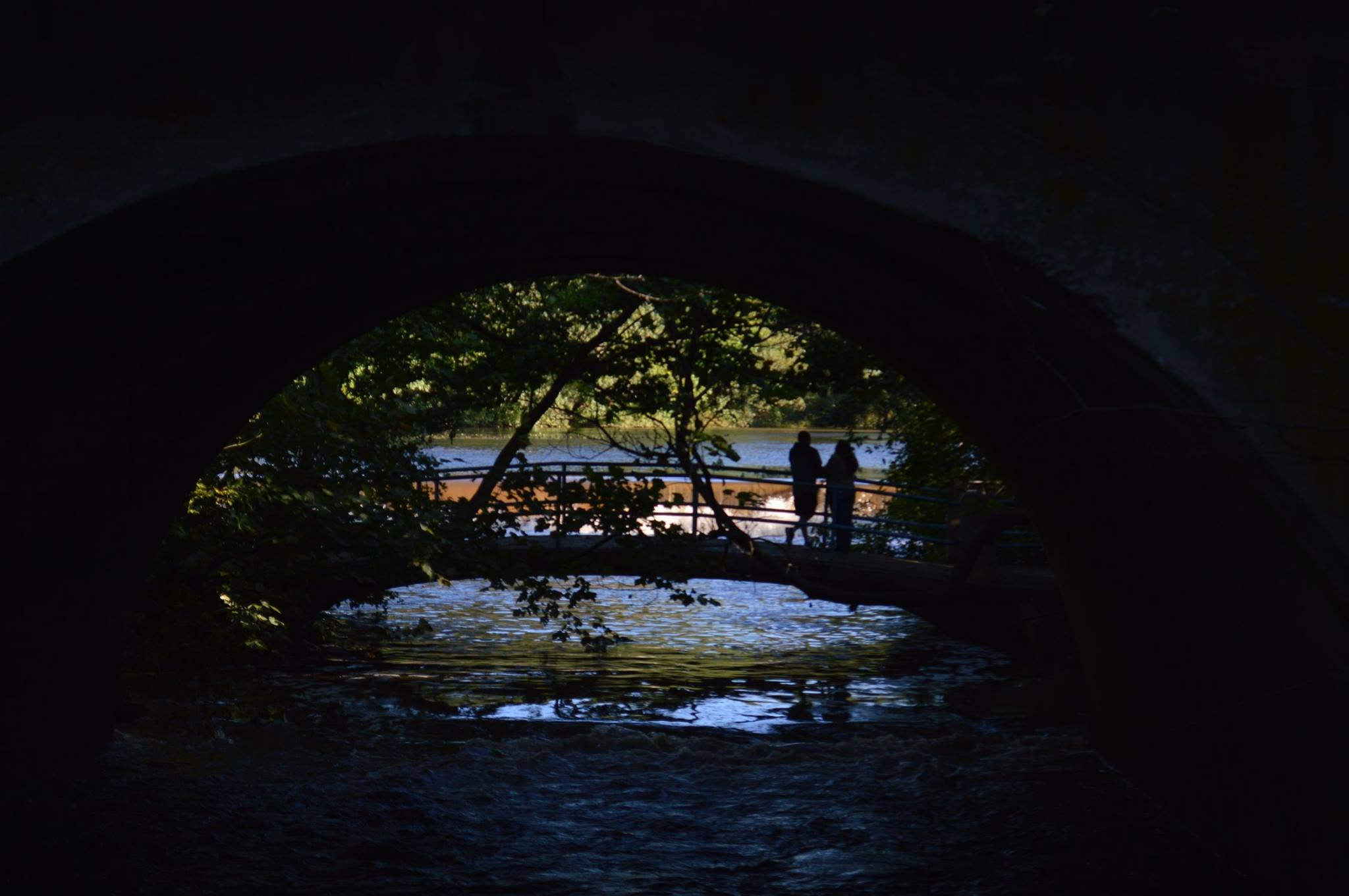 Two people beside the water, framed by a stone arch